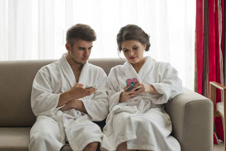 有吸引力的年轻夫妇穿着浴袍的沙发上看着智能手机