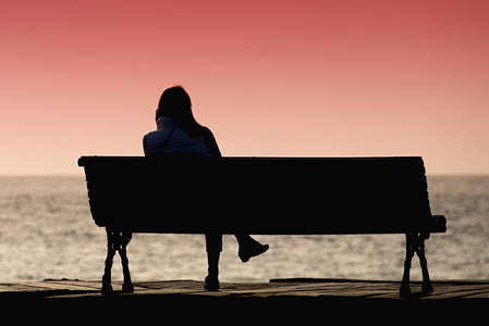年轻女子独自一人坐在长凳上的剪影