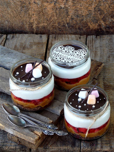 木制背景上的玻璃罐中的芝士蛋糕甜点 巧克力饼干 咸焦糖，草莓果冻，奶酪慕斯，巧克力镜子釉。选择性的焦点。复制空间