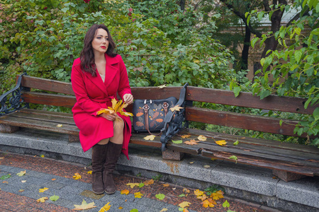 体贴的女子穿着红色的外套，在秋天的公园长凳上。人