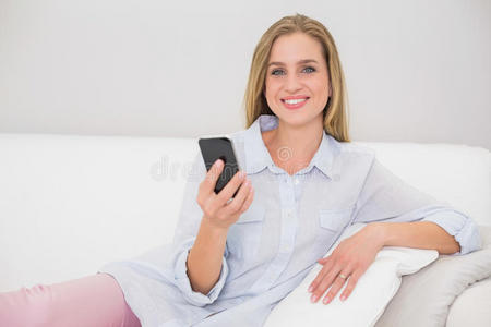 笑容可掬的金发女郎拿着智能手机在沙发上放松