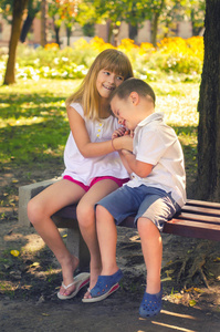 小男孩和小女孩在阳光灿烂的夏天一天坐在板凳上公园里玩