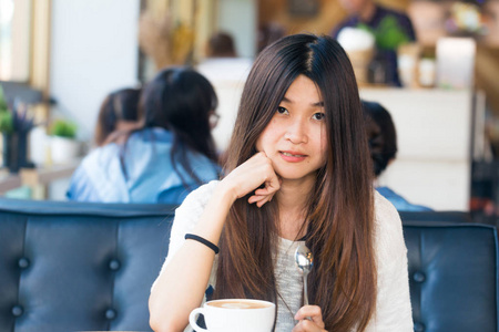 亚洲女性坐在图书馆里喝杯咖啡，为与人群一起创业树立一个想法