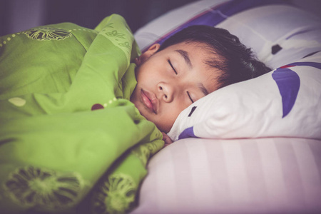 健康的孩子。小亚洲男孩平静地睡在床上。复古色调的作用