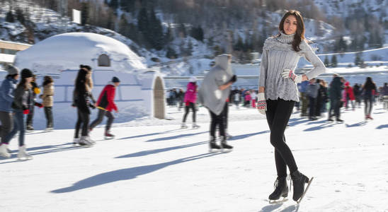 漂亮的女人滑冰冬天在户外，微笑面部。在背景中的山