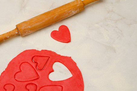 红色面团用擀面杖和切出的心在一个白色的表，特写。文本的空间