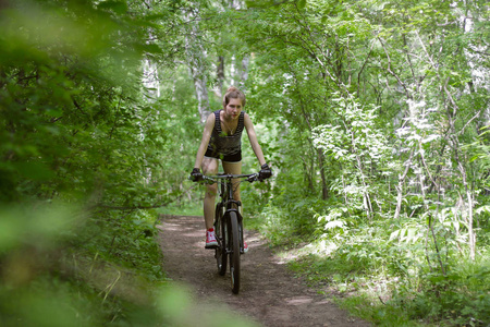 漂亮的女孩骑一辆山地自行车，穿过树林