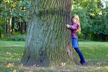 女孩在秋天的公园中拥抱一棵大树