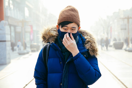 亚洲人走，戴着口罩的雾烟雾和朦胧的一天，因为他患有严重的空气污染在北京，中国