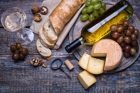 白葡萄酒中不少知识 软木 瓶螺杆和一套产品奶酪 葡萄 坚果 橄榄 无花果上一块木板，背景