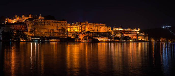 发光在乌代浦夜间的城市景观。宏伟的城市宫殿反射灯上皮丘拉湖，旅行的目的地在拉贾斯坦邦，印度