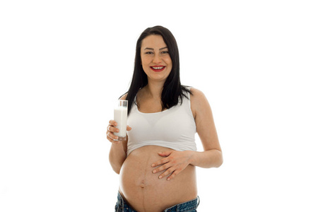 孤立在演播室里，笑着摆了杯牛奶中的白色背景上的年轻开朗的怀孕妈妈