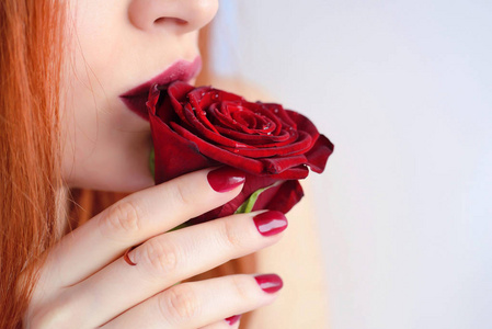 与红色玫瑰花的肖像。暗红色的嘴唇和指甲。年轻漂亮的红头发女人
