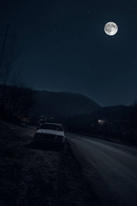 美丽的夜晚景观的大满月上升的山和树，与车路附近的山路