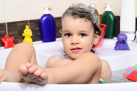 美丽的蹒跚学步，在浴缸中与泡沫洗个澡。可爱的孩子在洗澡洗他的头发用的洗发水和溅水无处不在