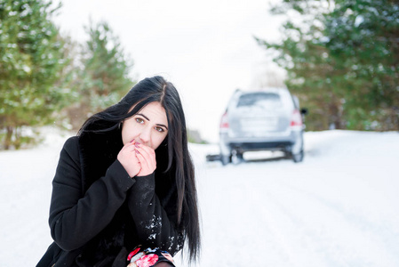 一个美丽的年轻女孩，他的车子抛锚在冬天森林里的肖像