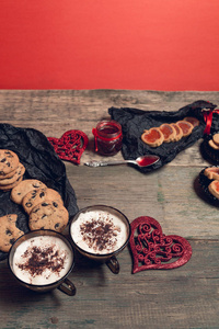 浪漫的早餐。两杯咖啡，卡布奇诺咖啡与巧克力曲奇饼和饼干附近红心木桌背景上。情人节的时候。爱。顶视图