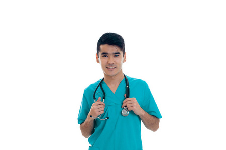 优雅的黑发年轻人医生的蓝制服，在听诊器摆姿势孤立在白色背景上