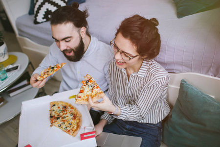 年轻的时髦男性女性夫妇家中吃披萨的笔记本电脑