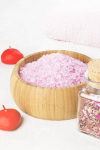 同在一个木碗 花瓣和新鲜的粉红色玫瑰玫瑰香气的沐浴盐 毛巾和白色背景上的蜡烛。色调
