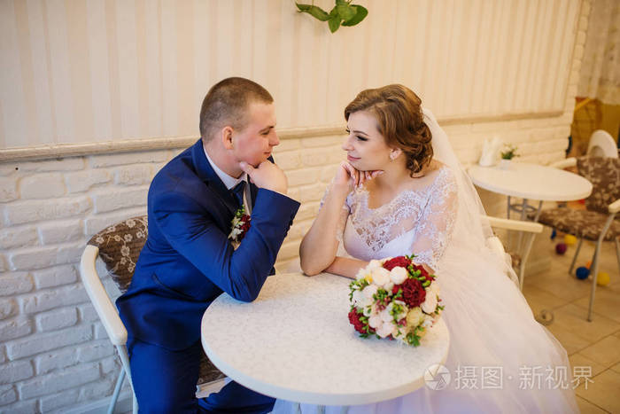 婚礼夫妇坐在咖啡馆的桌子旁手牵手