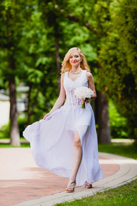 年轻美丽的新娘穿着白色的裙子在夏天公园散步