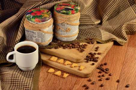 平静的生活与咖啡杯和两个装饰罐与咖啡豆，躺在一个木制的表面遮蔽格子毛毯。 饼干里的字母组合快乐的一天