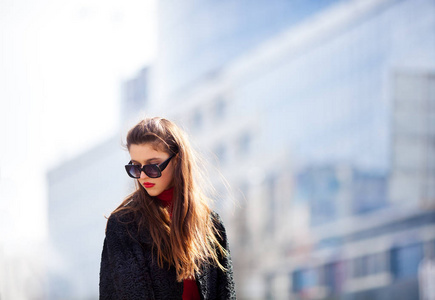 有吸引力的现代女性，站在城市街道上。时尚的年轻女人，戴着墨镜，黑色的衬衫和夹克