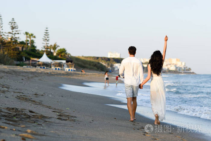 年轻幸福的夫妇在美丽的海滩散步
