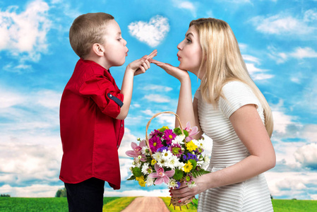 年轻美丽的母亲和儿子吹吻。一个女人和一个男孩与一束，一篮鲜花。春天的家庭度假和家庭之爱的概念。妇女节