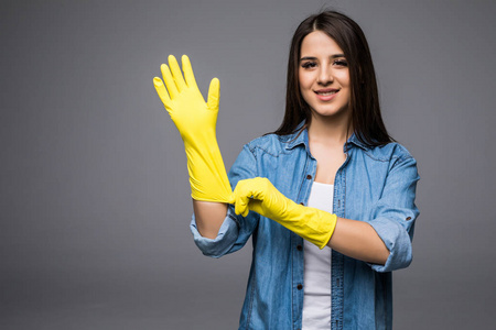 清洁女工获得春季大扫除准备戴上橡胶手套。清洁女工在相机上灰色背景孤立快乐的笑