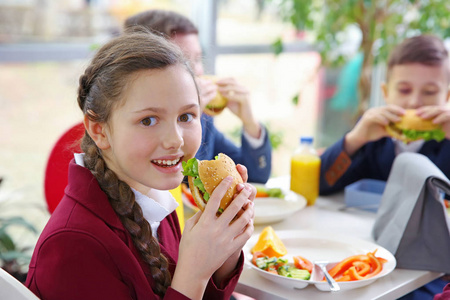 美丽的女孩一边吃着美味的食物，一边坐在学校食堂的餐桌上