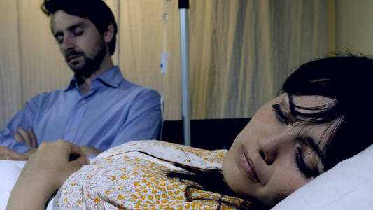 生病的女人伤心和沉思在医院与丈夫睡在她旁边