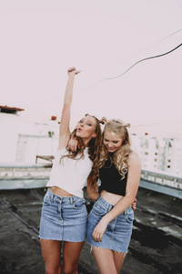 生活方式和人们观念 时尚肖像的两个时尚女孩最好的朋友在户外穿牛仔裙，在屋顶上。为了好玩的快乐夏季时间