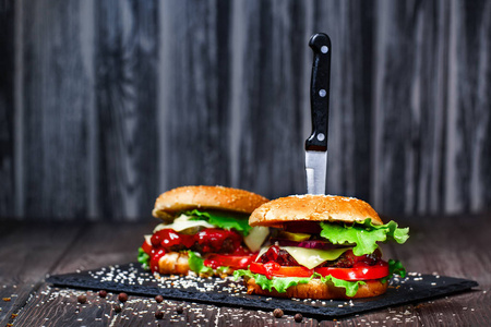 令人垂涎的美味的自制汉堡的一把刀的特写困在石材板。深色木背景