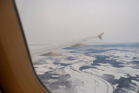 带着雪在陆地上空飞行。客机翼和冬季景观之下