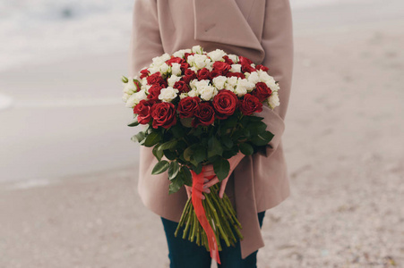 女孩拿着一份礼物的连接的磁带 红色和白色的玫瑰花束上中性的砂背景