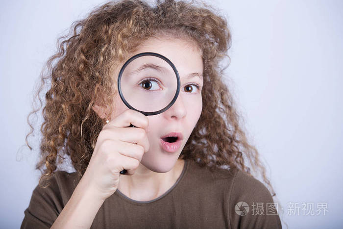 惊讶的可爱的小女孩,透过放大镜看画像