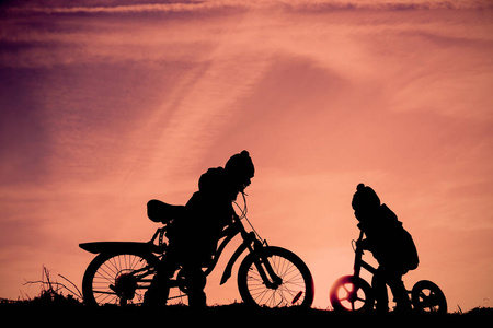 小男孩和女孩骑自行车在落日的天空