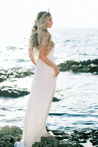 可爱的金发碧眼新娘的白色丝绸婚纱在海边摆姿势
