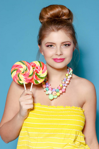 一个美丽的年轻女子用糖果在蓝色背景上的肖像。金发女郎，有着彩色的糖果。甜甜。聪明的女人