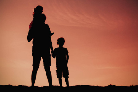 父亲与儿子和女儿在日落时的剪影步行