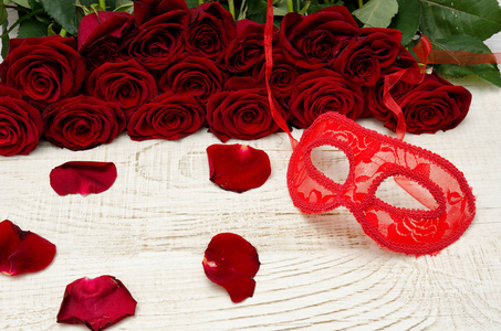 红色狂欢面具的猩红色玫瑰背景上木制的桌子上