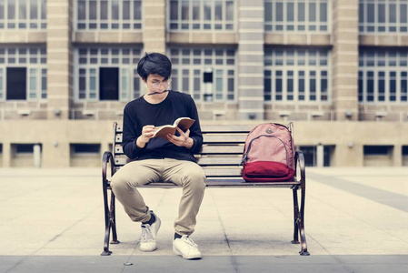 学生坐在长椅上，抱着笔记本