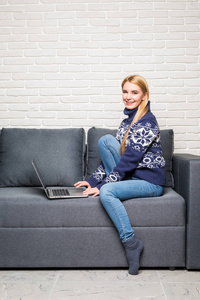 幸福的女人坐在沙发上，用她的笔记本电脑在家里，在客厅里