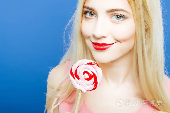 相机拿着棒棒糖在工作室中的蓝色背景上的手里可爱的小女孩糖果的肖像