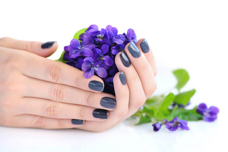 与黑暗修指甲指甲和束紫罗兰白色背景上一个女人的手