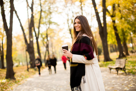 咖啡在秋天的公园里的年轻女子