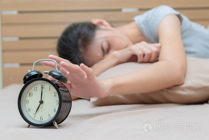 睡眼惺忪的年轻女子在床上,眼睛闭 ala 延伸手