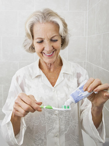 微笑的老太太在浴室用牙刷挤牙膏